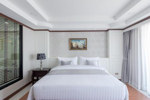 a white bedroom with a large bed and a window at Hotel de Ladda in Mukdahan