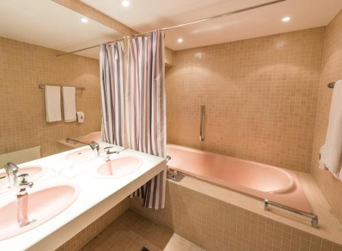 een badkamer met 2 wastafels en een roze bad bij Ascott Hotel & Restaurant in Rombach