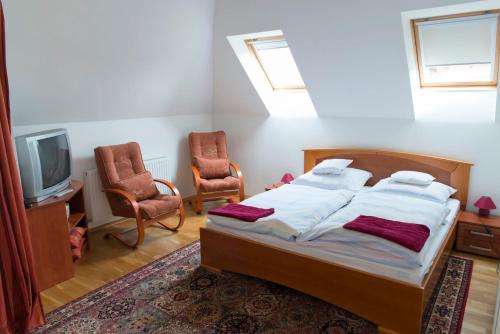 a bedroom with a bed and two chairs and a tv at Babos Panzio in Mosonmagyaróvár