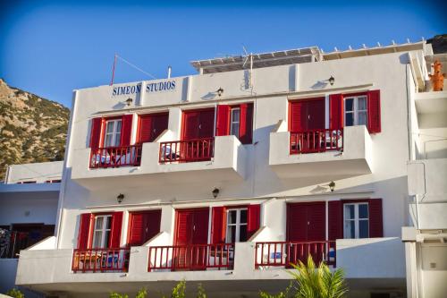 a white building with red shuttered windows and red shutters at Simeon Rooms & Apartments in Kamarai