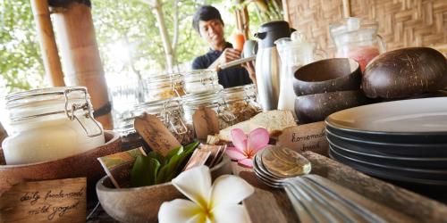 een man achter een tafel met borden, potten en bloemen bij Pearl Beach Resort Gili Asahan in Gili Asahan