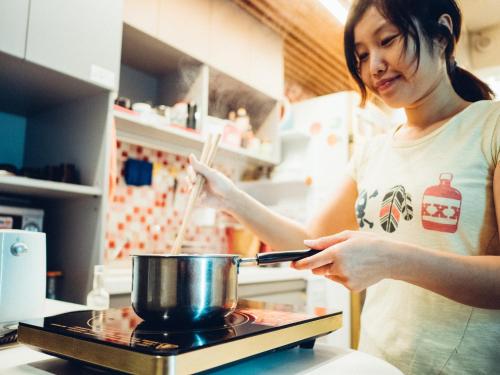 a woman stirring a pot with a pair of chopsticks at On My Way - Taipei Hostel in Taipei