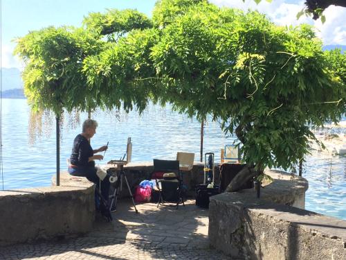 a man sitting at a desk under a tree next to the water at Appartamento Country House Menaggio in Menaggio