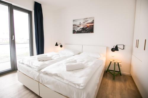 a white bed in a room with a large window at Hafenapartments Warnemünde in Warnemünde
