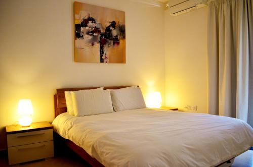 a bedroom with a white bed with two lamps at Hepburn Holiday Apartment in Birżebbuġa