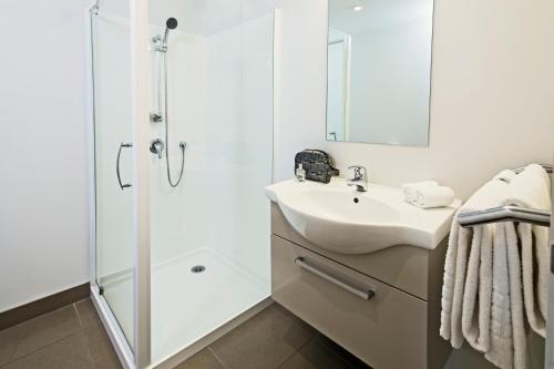 biała łazienka z prysznicem i umywalką w obiekcie Quest Albany Serviced Apartments w Auckland