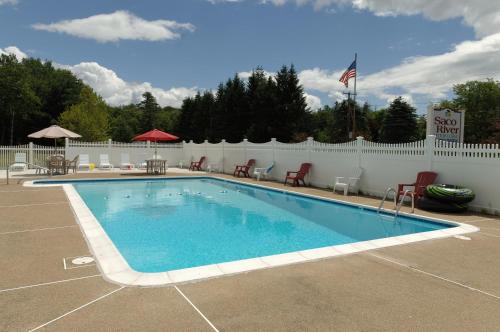 a swimming pool with chairs and a white fence at Saco River Motor Lodge & Suites in Center Conway