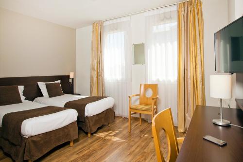 a hotel room with two beds and a desk at Séjours & Affaires Caen Le Clos Beaumois in Caen