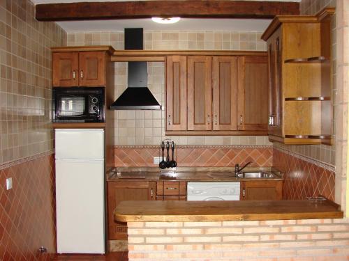 Una cocina con gabinetes de madera y un refrigerador blanco. en Apartamentos Sierra de Segura, en Segura de la Sierra