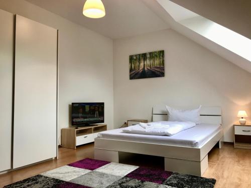 ein weißes Schlafzimmer mit einem Bett und einem TV in der Unterkunft Lokal Genial Pension & Restaurant in Beelitz
