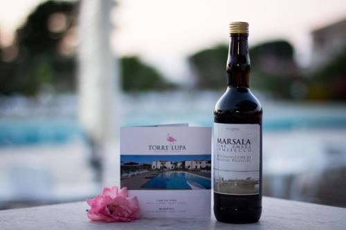 a bottle of wine sitting next to a pink flower at Case Vacanza Torre Lupa in Marsala