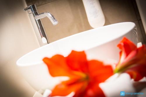 a bathroom sink with a red flower in a white holder at Hotel Amicizia in Rimini