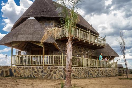 a building with a thatched roof and a palm tree at Big Valley Game Lodge in Lobatse