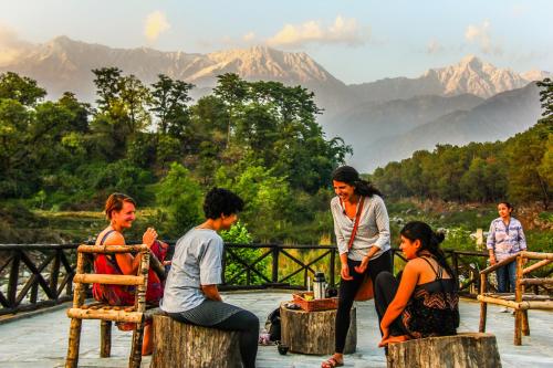 a group of people sitting on wooden chairs with mountains in the background at Prakriti Aalay - Riverside Mountain View Boutique Eco Resort in Dharamshala