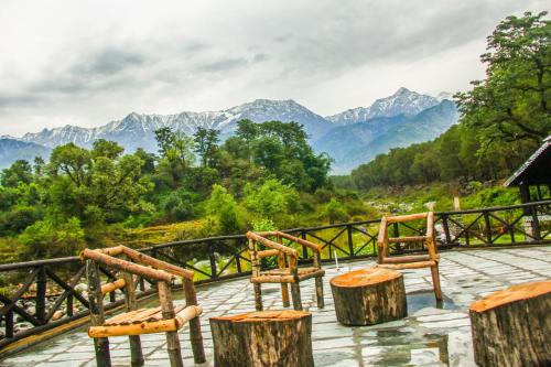 a group of chairs on a deck with mountains in the background at Prakriti Aalay - Riverside Mountain View Boutique Eco Resort in Dharamshala