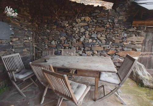a wooden table and chairs in front of a stone wall at Cabo Do Mundo Casa Rural in Chantada