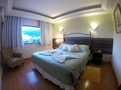 a bedroom with a bed and a chair and a window at Hotel Vila Nova in Teresópolis