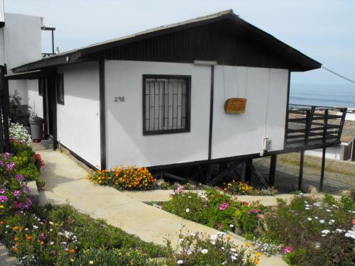 a small white building with a black roof and flowers at El Rincon de Las Pleyades in El Quisco