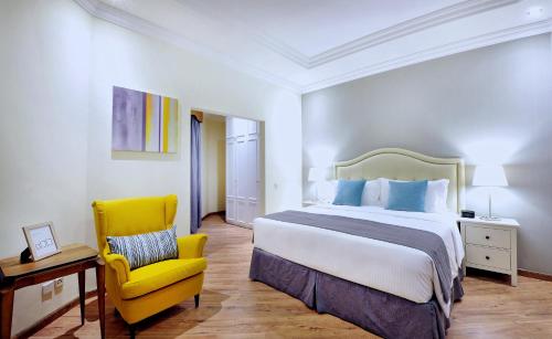 une chambre d'hôtel avec un lit et une chaise jaune dans l'établissement Spectrums Residence Jeddah, à Djeddah