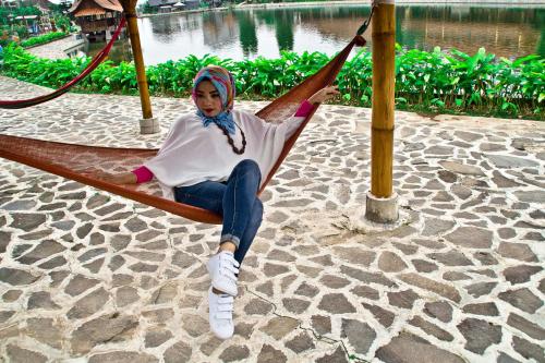 a woman is sitting in a hammock near the water at Puri Sakanti Nature Family Resort in Ciwidey