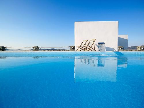 a pool of blue water with two chairs in front of a building at Lithos Luxury Rooms (Adults Only) in Adamantas