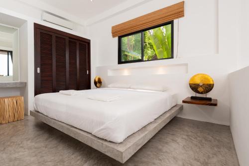 um quarto branco com uma cama grande e uma janela em The Plantation Koh Tao em Ko Tao