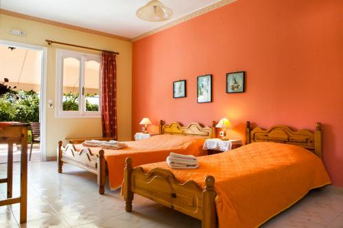 2 Betten in einem Zimmer mit orangefarbenen Wänden in der Unterkunft Tzivras Villa & Apartments in Lassi