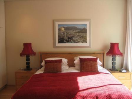 een slaapkamer met een rood bed met 2 lampen bij Navona Constantia Guest Cottage in Kaapstad