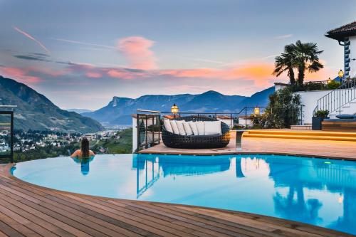 a woman sitting in the infinity pool of a house with a view of mountains at Golserhof in Tirolo