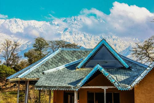 a house with a blue roof with mountains in the background at Prakriti Aalay - Riverside Mountain View Boutique Eco Resort in Dharamshala