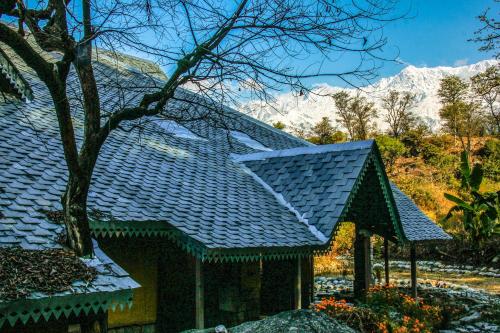 a house with a blue roof with mountains in the background at Prakriti Aalay - Riverside Mountain View Boutique Eco Resort in Dharamshala
