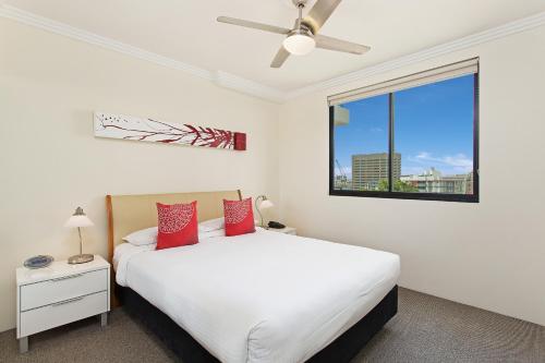 um quarto com uma cama branca com almofadas vermelhas e uma janela em Republic Apartments Brisbane City em Brisbane