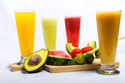 three glasses of juice and fruit on a cutting board at Fora Guest House Taman Lingkar in Bandung