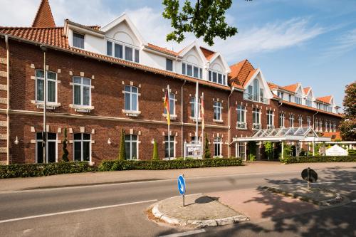 a large brick building with a blue sign in the street at Das 53°Hotel in Bad Zwischenahn