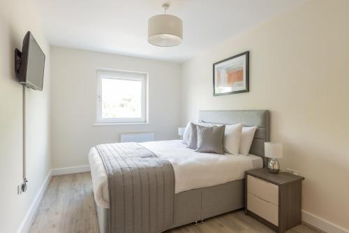 a white bedroom with a bed and a television at House of Fisher- Solstice House Apartments in Farnborough