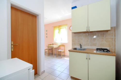 eine Küche mit weißen Schränken und einem Waschbecken und einem Tisch in der Unterkunft Apartments Antea in Rogoznica