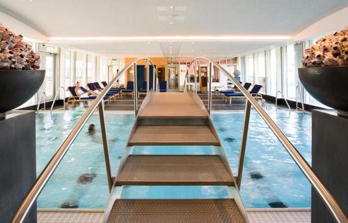 an indoor swimming pool with stairs in a building at Steigenberger Airport Hotel Amsterdam in Schiphol
