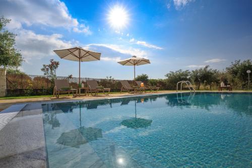a swimming pool with two umbrellas and chairs and a table at Skales Villas in Almiros Beach