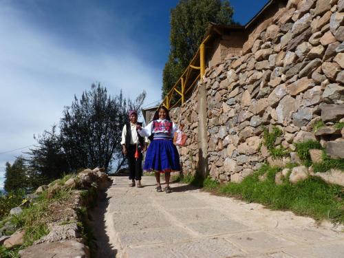 two people walking down a path next to a stone wall at Amantani Lodge in Amantani