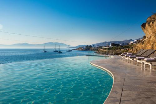 a swimming pool next to the water with lounge chairs at Mykonos Beach Hotel in Mýkonos City