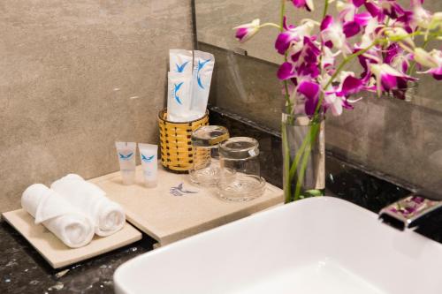 a bathroom counter with towels and a vase with flowers at Apus Hotel in Nha Trang