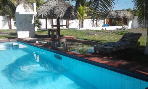 a blue swimming pool with a bench and a umbrella at Villa Tortugas in Monterrico