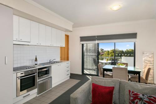 a kitchen with white cabinets and a dining room with a table at Quest on Rheola in Perth