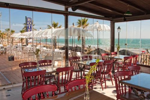 a restaurant with tables and chairs and the ocean at Hotel Playa de Regla in Chipiona