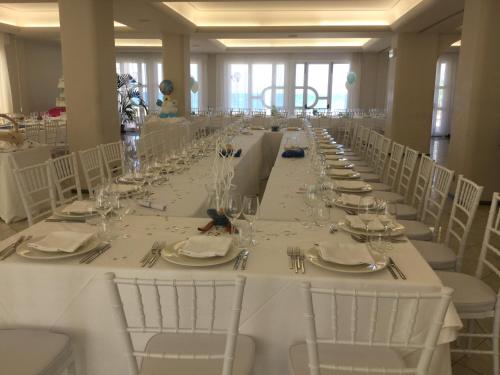 un lungo tavolo con tavoli bianchi e sedie bianche di L'Approdo di Angelino a Pizzolungo