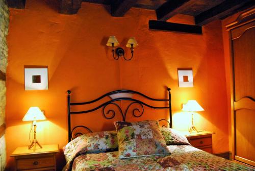 a bedroom with an orange wall with a bed and two lamps at Casa Azon in Oliván