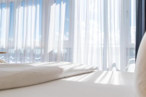a white bed with white curtains in front of a window at Strand-Hotel Hübner in Warnemünde