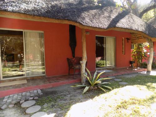 a small red house with a thatch roof at Jump Street Chalets in Maun