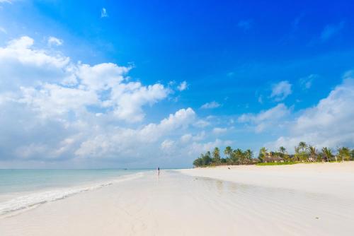 a beach with a person walking on the sand at The Sands Beach Resort in Bwejuu