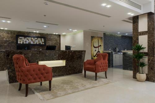 アル・ジュバイルにあるRemaz Suites Hotelの赤い椅子2脚とカウンターのあるロビー